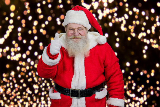 Happy Santa giving thumb up. Kind Santa Claus showing gesture ok on New Year lights. Realistic Santa Claus, portrait.