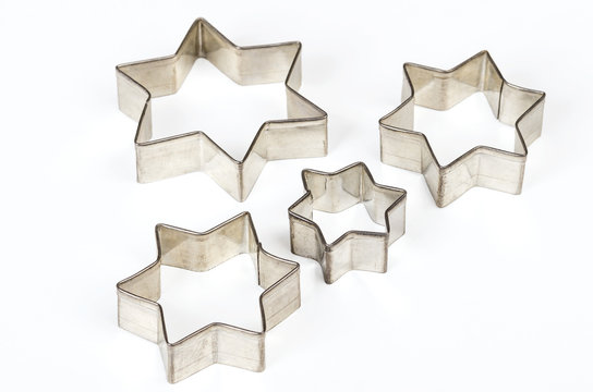 Four star shaped Christmas cookie cutters over white. Tin biscuit cutters, tool to cut cookie dough in particular shapes and to make cutouts. Hexagram shaped and six pointed geometric star figures.
