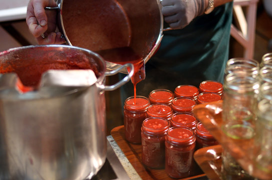 Marmelade wird aus einem silbernen Topf in Einweckgl&auml;ser abgef&uuml;llt