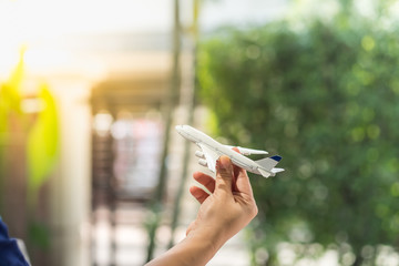 Transportation and travel concept. Close up of woman hand holding airplane toy model with garden view as background.