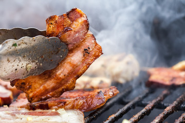 Barbecue de bacon dans des pinces métalliques close up