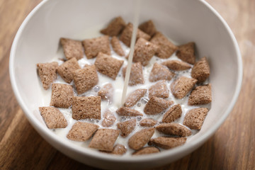 pouring milk into chcolate cereal pillow in white bowl on table