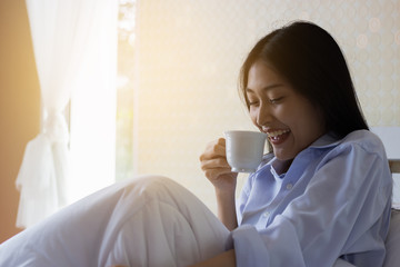 Happy Asian woman drinking coffee on bed