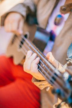 Closeup of young man hands playing acoustic bass guitar ukulele at the park sit Enjoy living Sunshine in the evening.