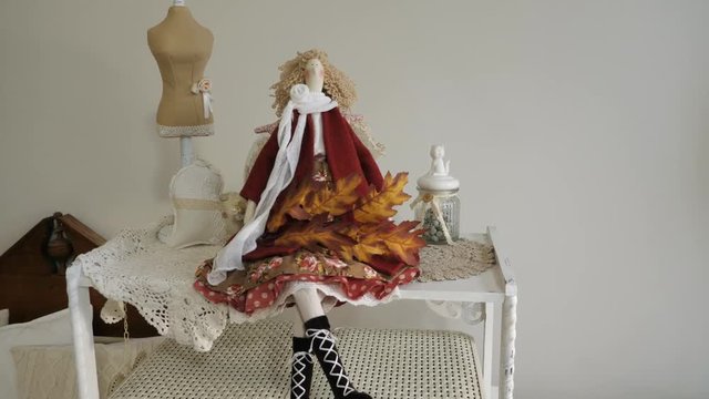 A beautiful doll sits on a shelf with a maple branch.