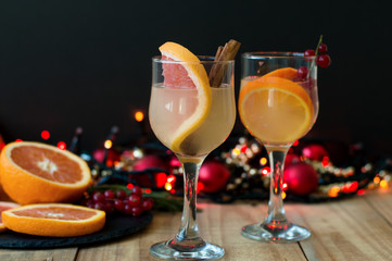 Winter cocktail with grapefruit, cinamon and red currant in wine glasses served with christmas decoration: lights and red balls on black background
