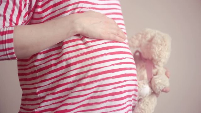 Pregnant woman holding plush toy and touching her belly with hands