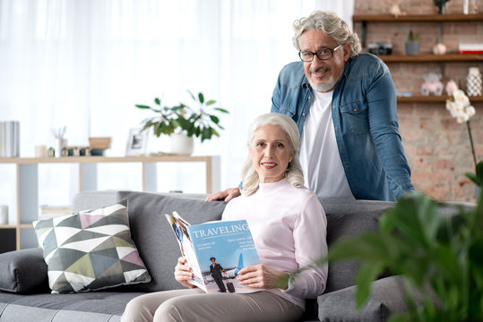 Cheerful senior married couple reading magazine in living room