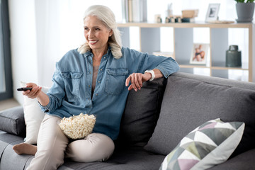 Fototapeta premium Joyful mature lady entertaining with television in living room