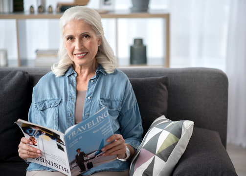 Happy mature woman reading magazine in living room