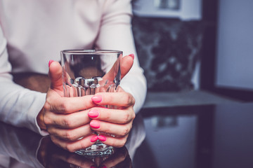 Holding an empty glass in hands. A woman is holding her hands on a table, squeezing an empty glass. Waiting for drink, conversation, waiting for something, concept.