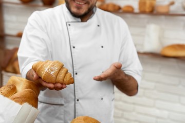 Cropped shot of a cheerful professional baker smiling holding out delicious fresh croissant offering to the viewer copyspace breakfast sweet dessert sugar eating bakery concept.