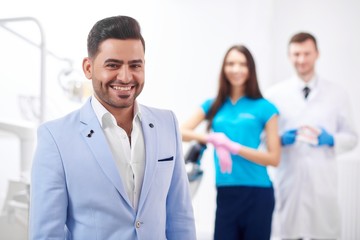 Happy handsome male businessman smiling to the camera standing at the dentist office his doctor and nurse posing on the background copyspace healthcare medicine dentistry service concept.