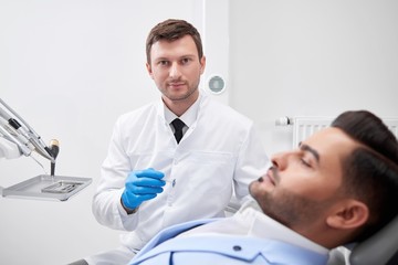 Fototapeta premium Mature male dentist looking to the camera confidently while working with his patient dentistry oral checkup doctor profession experience occupation healthcare medicine concept.