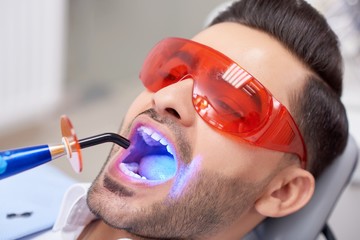 Close up portrait of a handsome young man wearing protective eyewear getting teeth filling done at the dental clinic professionalism safety healthcare medicine smile treatment dentistry.