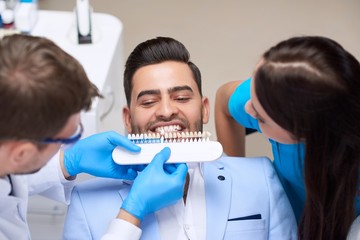 Top view shot of a profesisonal dentist wirking with assistance of the nurse choosing perfect matching color of implants for his male patient teeth medicine healthcare whitening dentures.