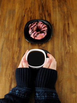 Doughnut with glazing and a cup of coffee in woman`s hands
