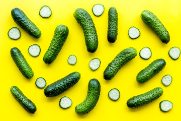 Fresh cucumber pattern. Whole and slices cucumbers on yellow background top view