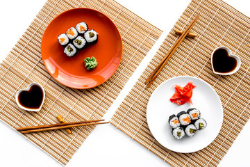 Fototapeta na wymiar Sushi roll with salmon and avocado on plate with soy sauce, chopstick, wasabi on mat. White background Top view