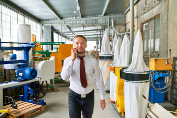 Portrait of successful shop consultant wearing suit posing looking at camera, standing by machine tools in industrial  showroom and speaking by phone smiling happily