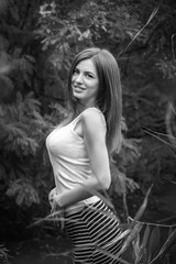 Obraz na płótnie Canvas Black and white portrait of beautiful young smiling woman with long hair, wearing long striped skirt and white top standing in a forest