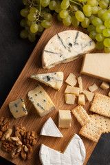 Tasting cheese dish on a wooden plate. Food for wine and romantic, cheese delicatessen on a dark stone table. Top view