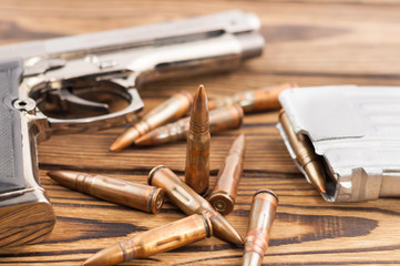 Single metal glossy pistol and silver magazine with scattered bullets for assault rifle on old rustic wooden weathered planks