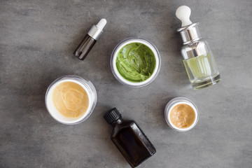 Bottles and jars with natural skincare cosmetics, creams and oils on dark background. Plant-based beauty products. Top view