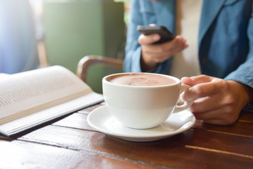 Woman Hands holding cup of coffee and using smart phone.