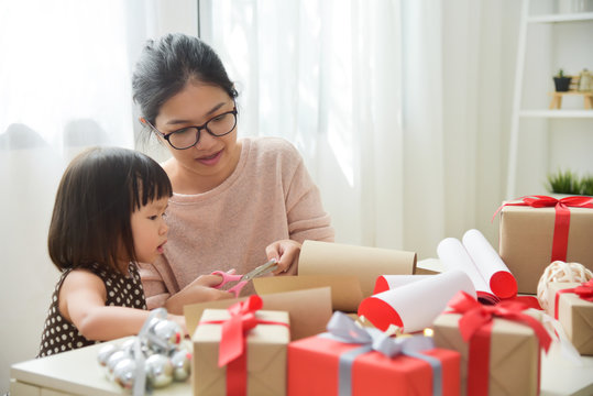 Young Mother And Her Daughter Wrapping Gift Boxes.