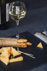 Cheese plate served with crackers and glass of white wine on dark background.