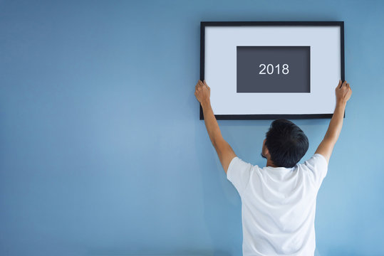 New year concept. Asian man holding a picture frame of 2018 on blue wall.