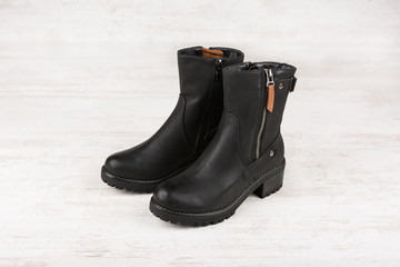 Female winter leather shoes on white wooden background.