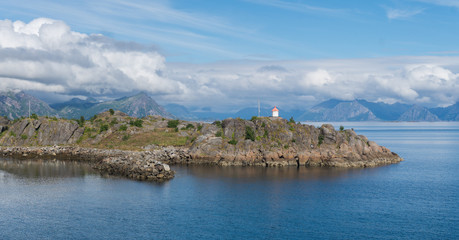 Naklejka premium Lighthouse on a rocky cape on a background of mountains, Lofoten, Norway