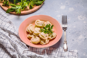 Boiled dumplings in a pink plate on a gray background, parsley, horizontal