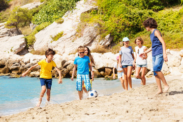 Kids play soccer ball on the sea beach