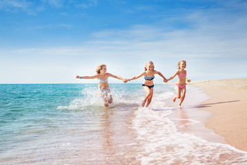 Girls running in sand and waves of sunny beach