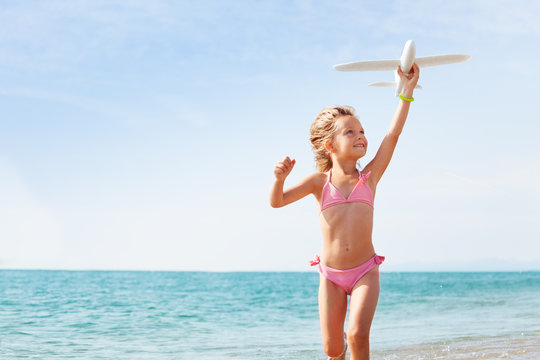 Happy girl playing with toy plane on the seashore