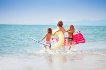 Three girls with swimming tools running to the sea