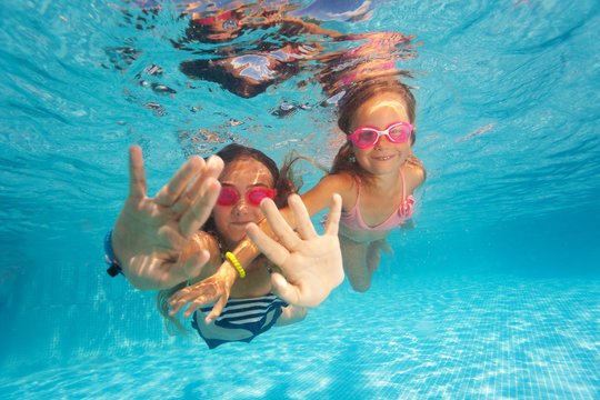 Two happy girls swimming under clear water of pool