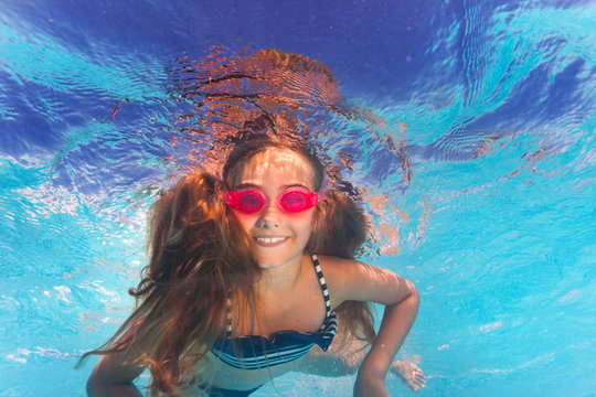 Happy girl in pink goggles swimming under water