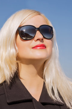 Closeup shot of blonde model  wears sunglasses, posing in black coat in sun light