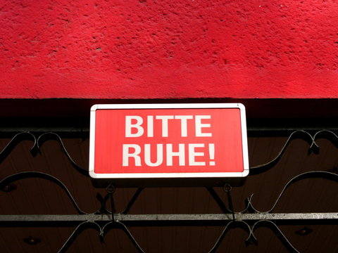 Rotes Hinweisschild Bitte Ruhe! am Eingang eines Nachtclub mit roter Fassade und schwarzem Eisengitter bei Sonnenschein in K&ouml;ln am Rhein in Nordrhein-Westfalen