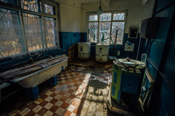 Sinister and creepy old laundry room with a dirty floor and broken wash machines and bathes in an abandoned psychiatric hospital.
