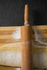 Close up of rolling pin on dough over cutting board