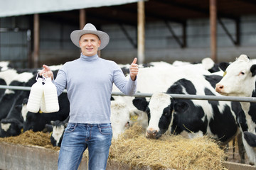 positive farmer with milk on background of cow farm