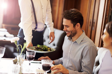 Romantic couple dating in restaurant being served by waiter