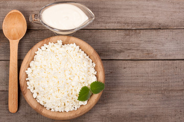 Cottage cheese in a wooden bowl with sour cream on old wooden background with copy space for your text. Top view