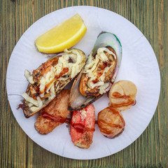 Several fried mussels, two piece of crab meat and several deep-sea scallops with lemon lie on a paper plate as an expensive fast food