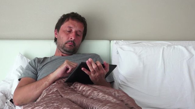 Using digital tablet for social network activities in bedroom, man with portable touchscreen computer device in bed.